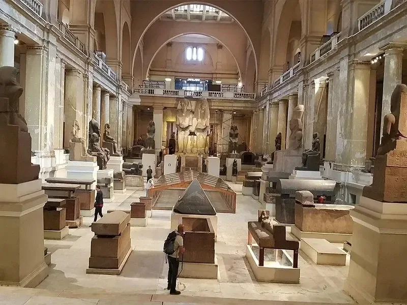 The grand interior hall of the Egyptian Museum in Cairo, lined with ancient statues, sarcophagi, and stone artifacts on display.