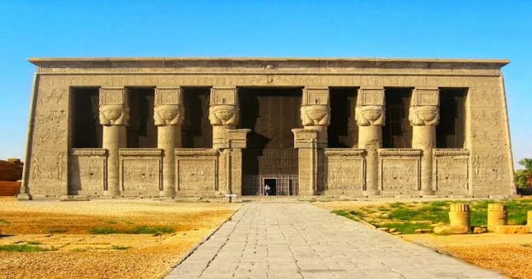 Stone pathway leads to the imposing facade of Dendera Temple with rows of Hathor-headed columns.