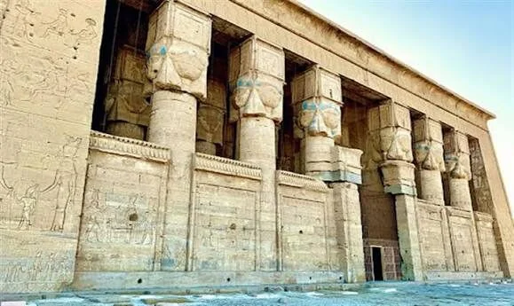 Close-up of carved stone columns topped with Hathor-head capitals along the temple's front wall.