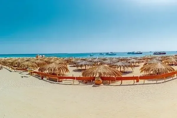 Panoramic view of straw beach umbrellas lined along the shoreline with tour boats anchored offshore.