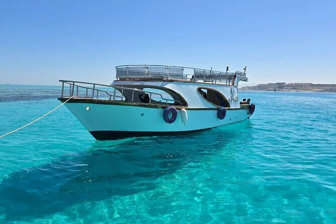 White and dark-blue glass-bottom boat with an open upper deck anchored in bright turquoise water.