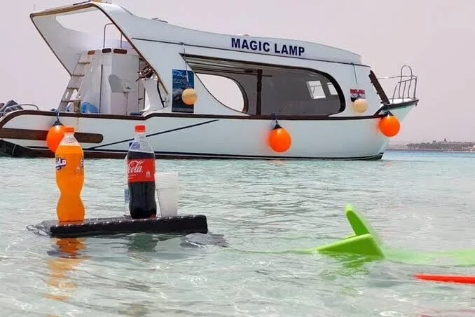 Boat named Magic Lamp moored in shallow water with soft drink bottles and cups set on a small floating tray table.