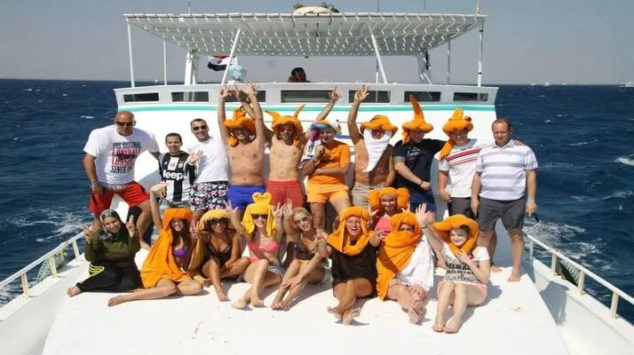 A large group in matching orange hats posing together on the bow of a boat.