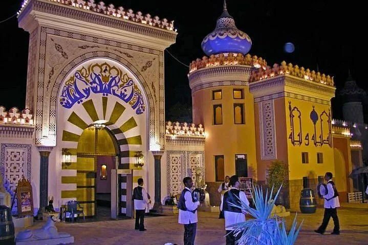 An ornate illuminated Arabian-style gateway and towers at night, with staff walking near the entrance.