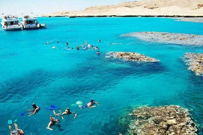 Aerial view of snorkelers swimming over coral patches in turquoise water near two anchored dive boats.