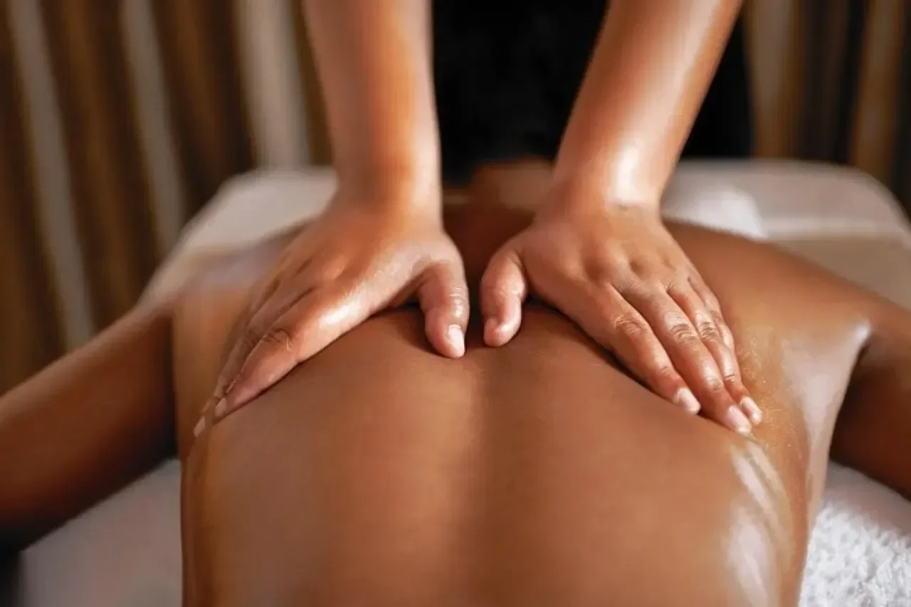 Close-up of two hands massaging a client's oiled bare back on a treatment table.