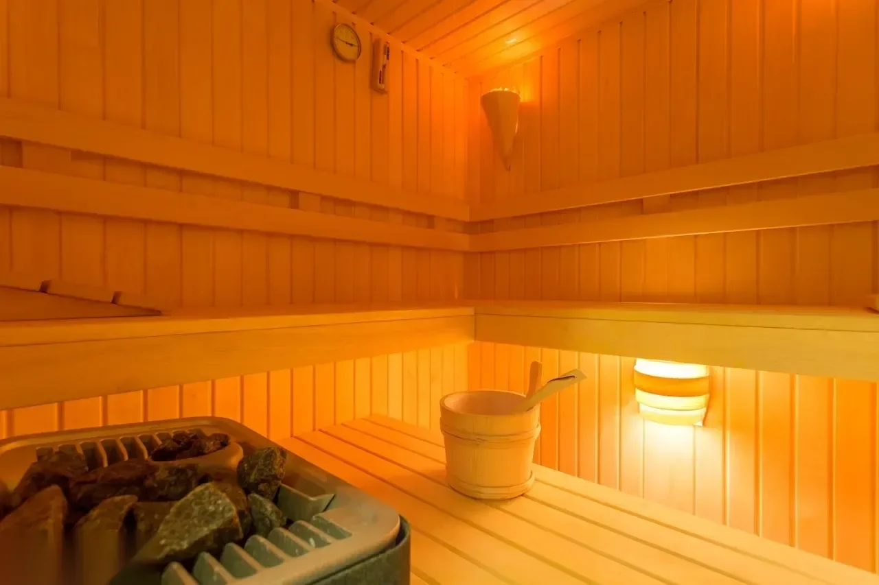 Interior of an empty wooden sauna with a bucket, ladle, hot stones, and a wall clock.