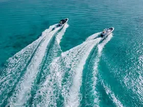 An aerial view shows two speedboats racing side by side across turquoise water, leaving parallel white wakes.
