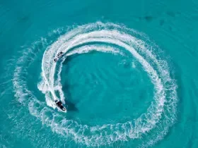 An aerial view shows a speedboat carving a tight circular wake in turquoise water.