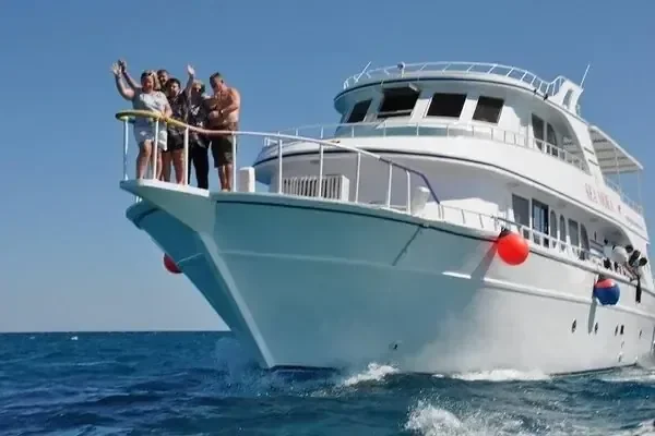 A group of guests wave and pose on the bow of a large white tour yacht as it cruises.