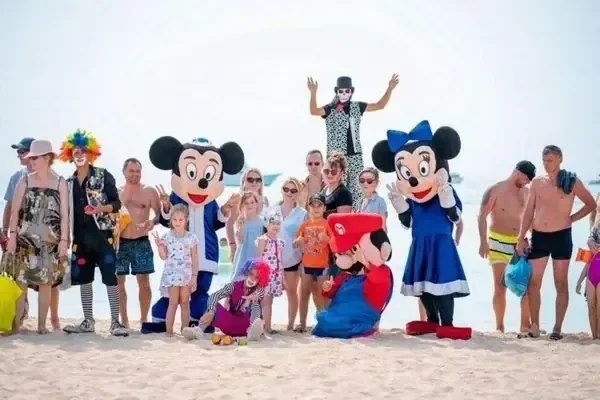 A group of tourists poses on the beach with people dressed as Mickey Mouse, Minnie Mouse and other cartoon characters.