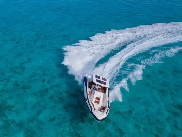 Aerial view of a speedboat carving a wide white wake through turquoise sea.