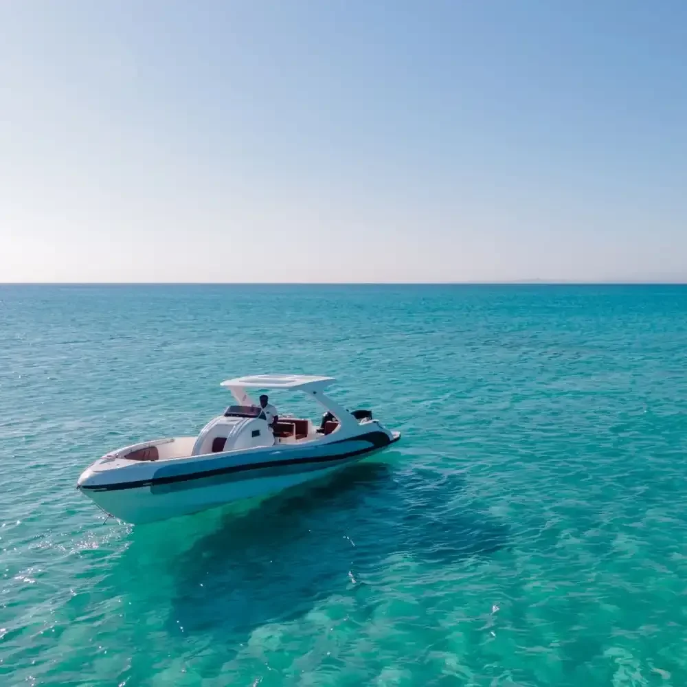An empty white speedboat with a sun canopy drifts on calm turquoise water, a lone driver seated at the wheel.