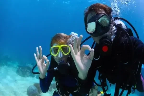 Two scuba divers underwater making the 'okay' hand signal at the camera.