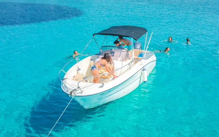 A woman relaxes on the bow of an anchored speedboat while others swim nearby in clear turquoise water.