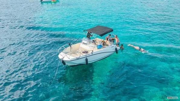 Passengers sit aboard a moored speedboat as one person dives off the side into the sea.