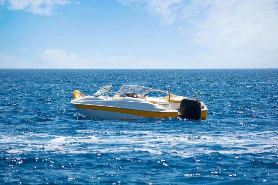 A yellow-and-white speedboat sits idling alone on calm open blue water.