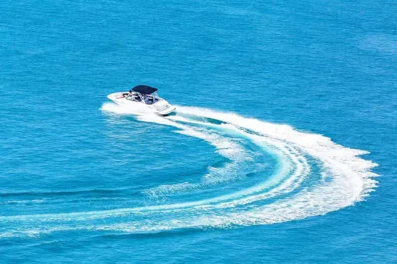 Aerial view of a speedboat carving a wide curved white wake across turquoise sea.