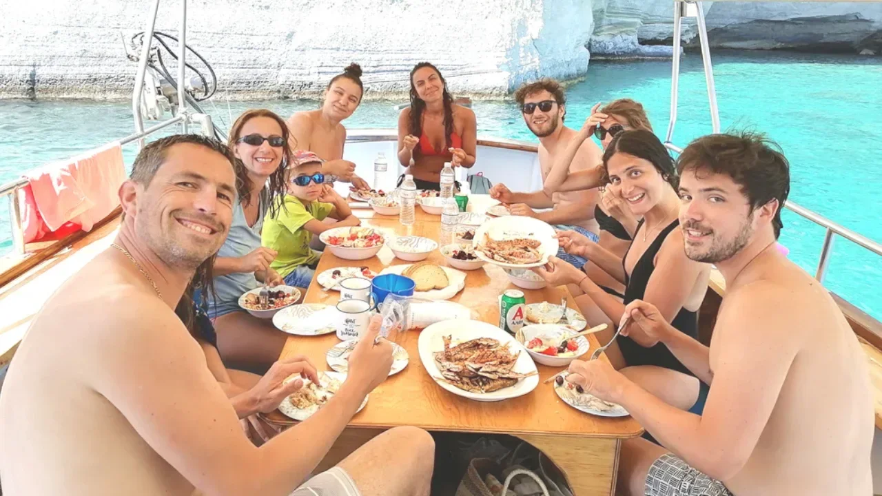 A group in swimwear serves themselves from a buffet of rice, vegetables, grilled meat and fresh fruit laid out on a dive boat, with scuba fins hanging on the rail.