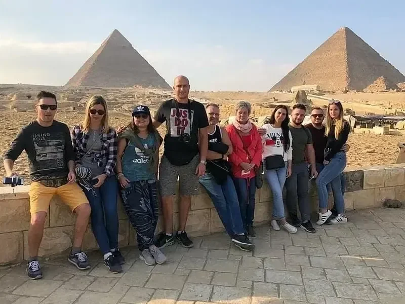 Large group of ten tourists posing together in front of the two Great Pyramids of Giza.