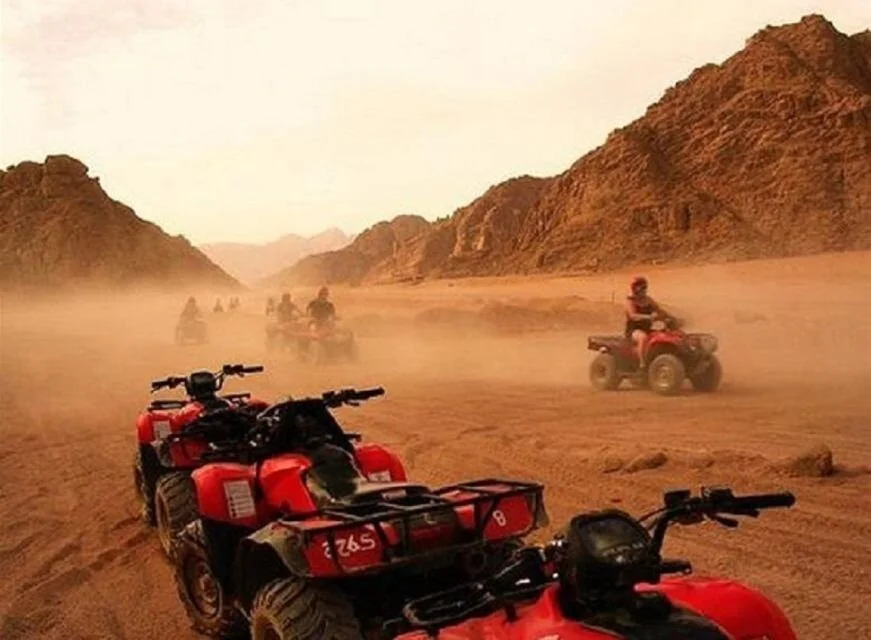 Close-up of red quad bikes lined up with riders heading off into a cloud of dust in a mountain valley.