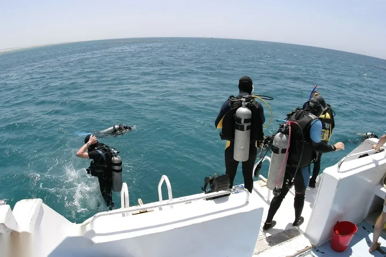Divers enter the water from a dive boat platform, one already submerged and others waiting with tanks on.