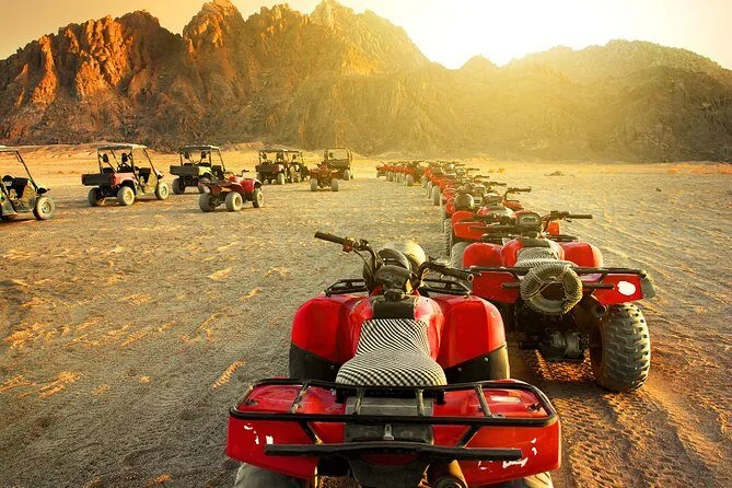 Row of red quad bikes lined up in the desert with mountains glowing at golden hour