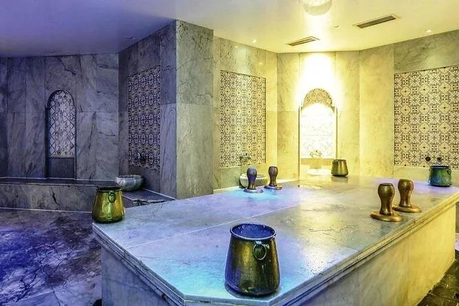 Hammam washing room with marble walls, decorative mosaic tile niches, and brass wash basins arranged on a marble bench
